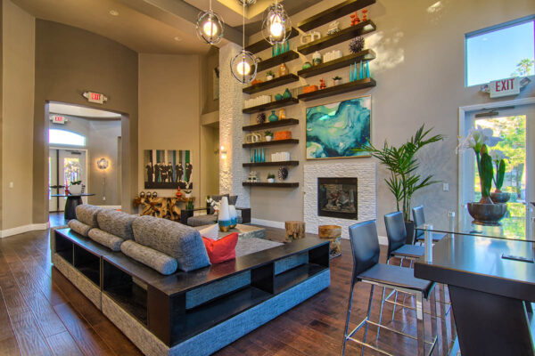 Clubhouse with plush seating, large fireplace, shelves with decor, and two story windows.