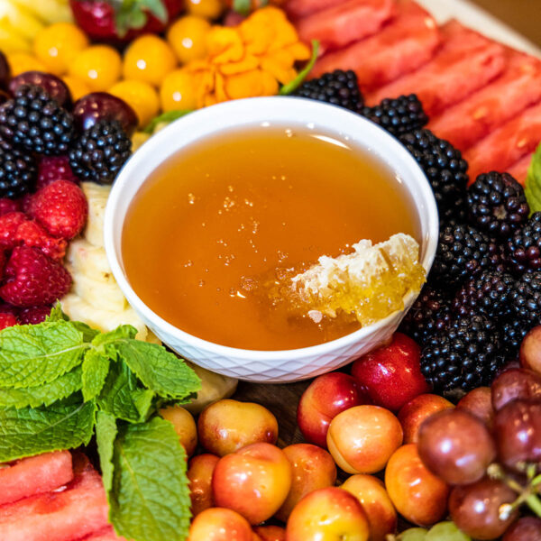 Fruit tray with berries, watermelon, grapes, and bowl of honey.
