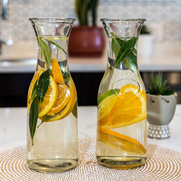 Carafes of water with fruit and herbs on counter.