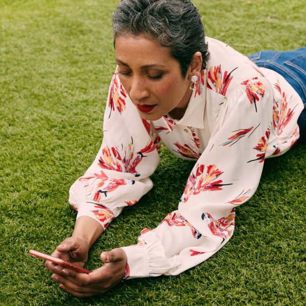 Older person in pattern shirt laying on grass with smart phone.