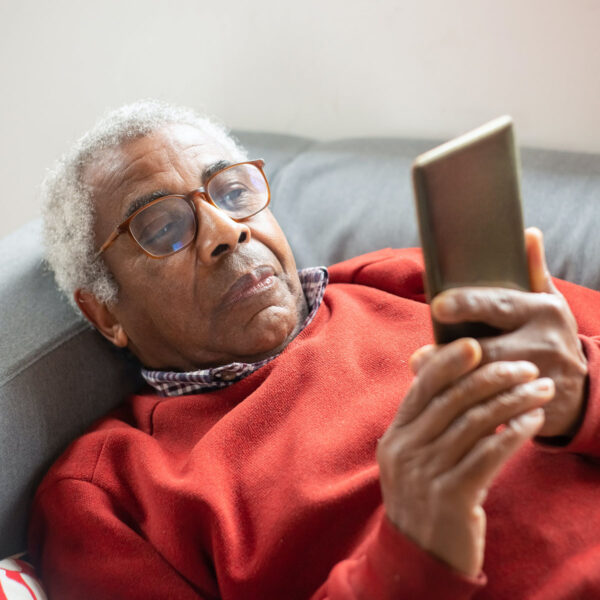 Older person laying on couch looking at smart phone.