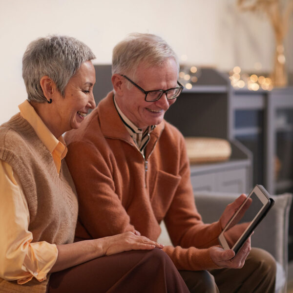 Older couple laughing together looking at tablet.