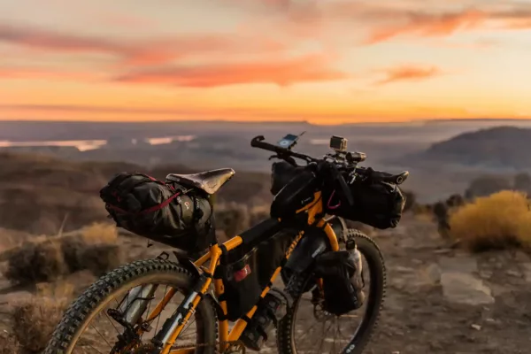 Mountain bike with gear bags parked on rocky mountaintop at sunset.