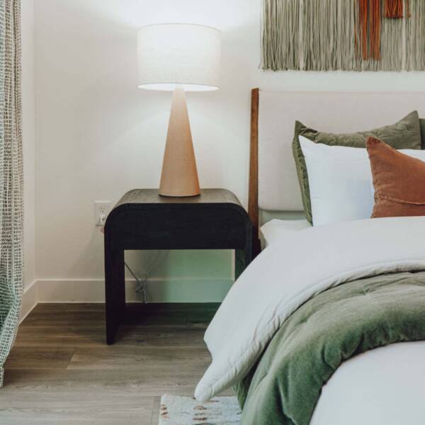 Bedroom with plush bed, wood style floor, and bedside table with lamp.