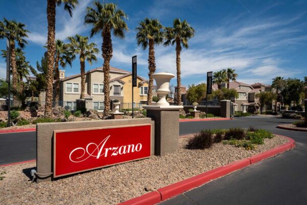 Arzano apartments monument signage with rocky landscaping and palm trees.