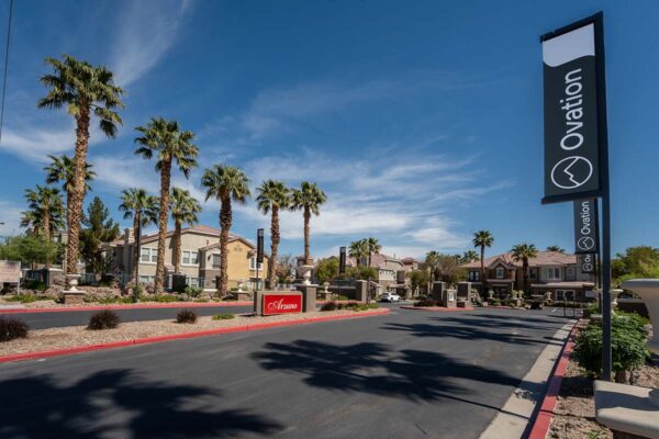 Arzano apartments entrance with monument sign, rocky landscaping, and palm trees.