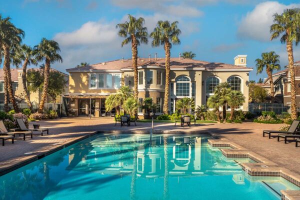 Arzano apartments pool area with lounge chairs and tall palm trees.