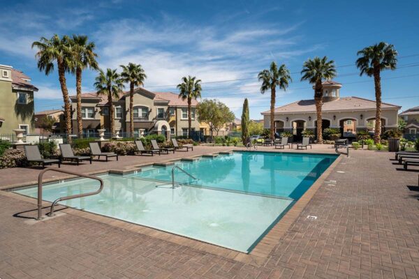 Arzano apartments pool area with lounge chairs and tall palm trees.