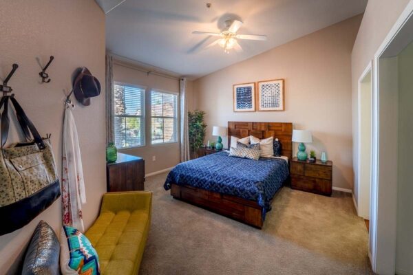 Arzano apartment bedroom with carpet, plush bed with headboard, bedside tables with lamps, and large windows.