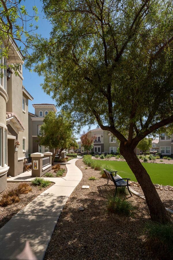 Arzano apartments courtyard with grass, rocky landscaping, and tall trees.