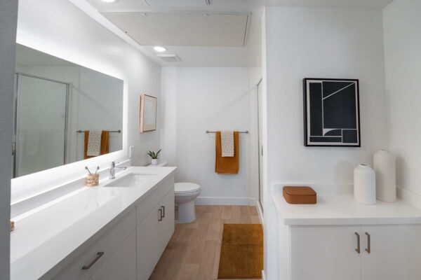 Arzano apartment bathroom with wood style floor, white cabinets, lighted mirror, and orange decor.