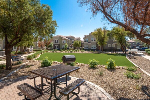 Arzano apartments common area with lush green lawn, BBQ grill, and dining table.