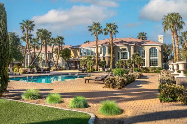 Arzano apartments pool area with lounge chairs, lush landscaping, and tall palm trees.