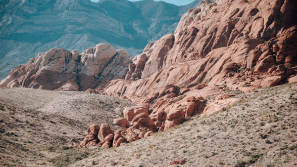 Vibrant red sandstone rock formations set against a backdrop of blue-toned rugged mountains.
